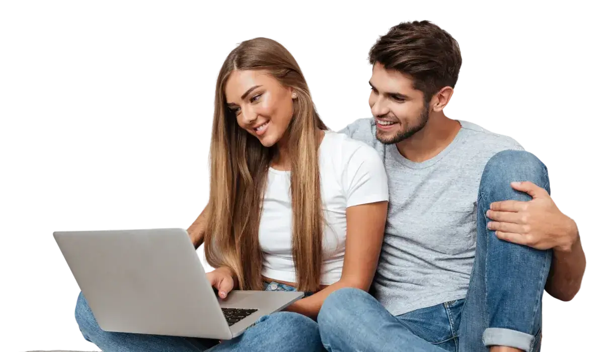 A young man and woman sitting together, smiling as they look at a laptop screen, exploring interior design ideas. Both are casually dressed and appear engaged and happy.