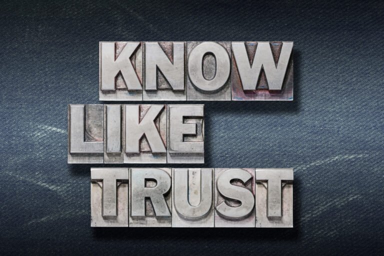 Metallic printing blocks spelling out "Know, Like, and Trust" on a dark textured background.