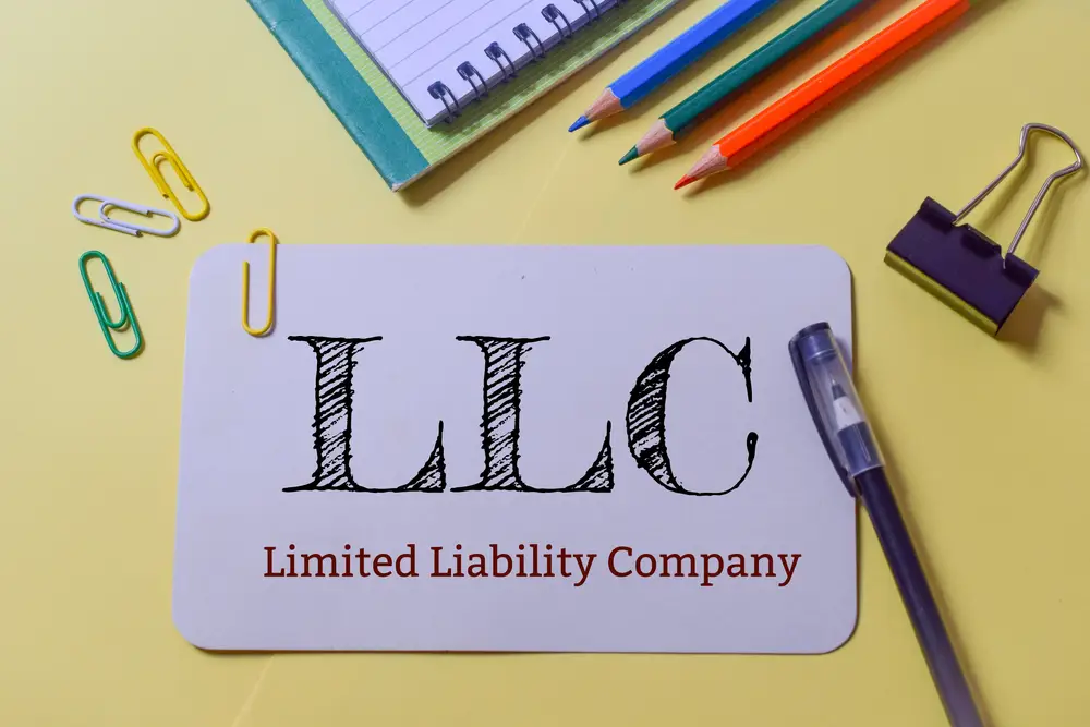 A "LLC Limited Liability Company" card sits on a desk surrounded by colorful paperclips, pencils, a pen, and a notebook—tools for smart business planning.