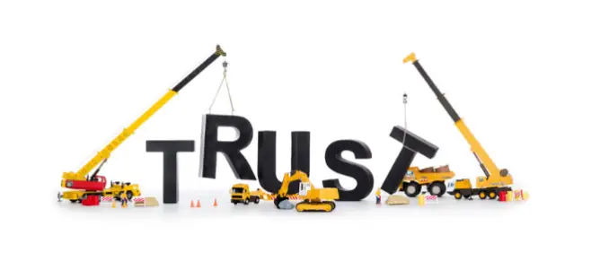 Giant black letters spelling "TRUST" are expertly assembled by two cranes and construction vehicles against a pristine white background, symbolizing the foundational role of trust in driving profit through effective affiliate marketing strategies.